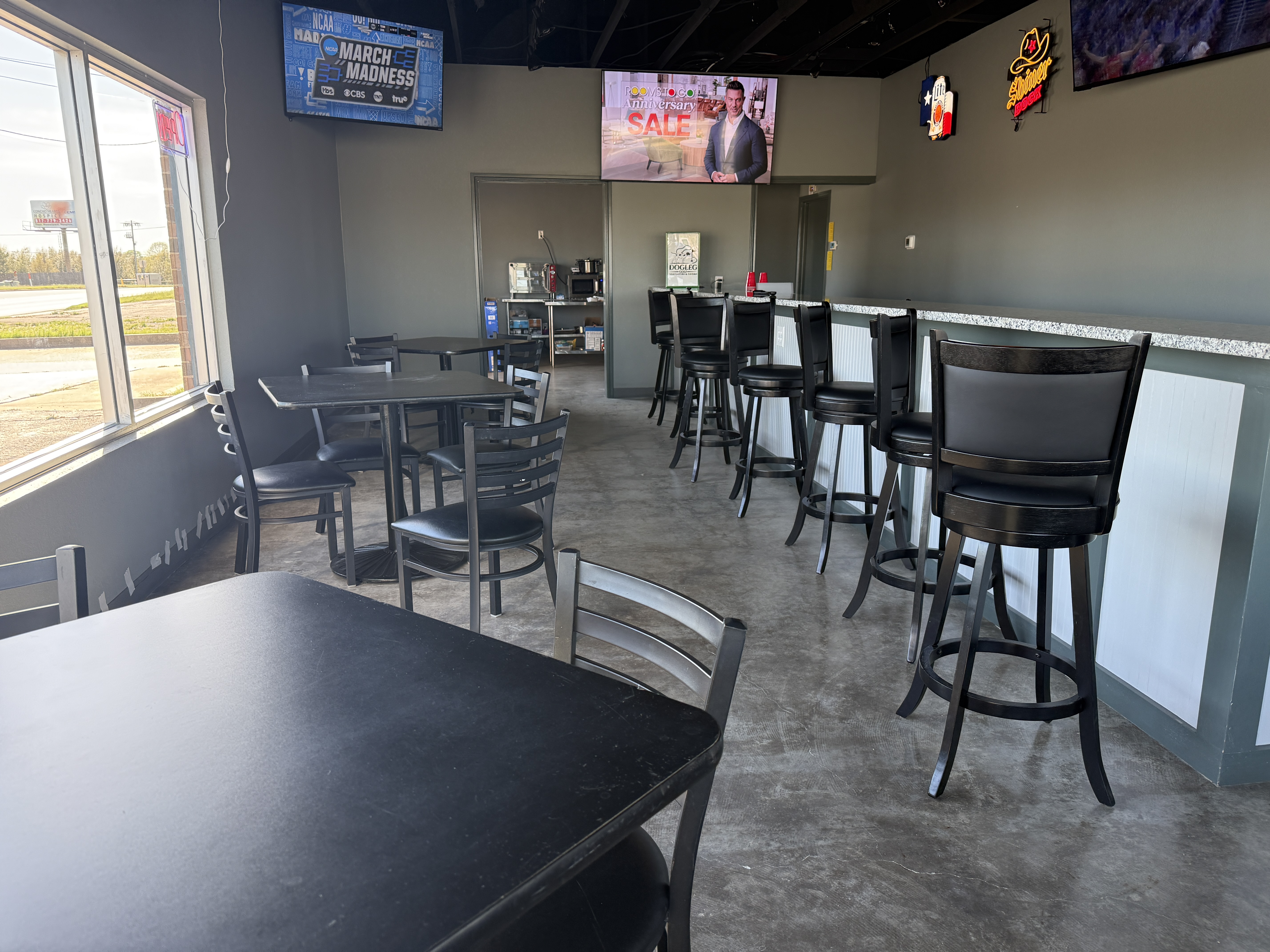 Dining area with tables, barstools, and TVs showing the game at Dogleg Golf