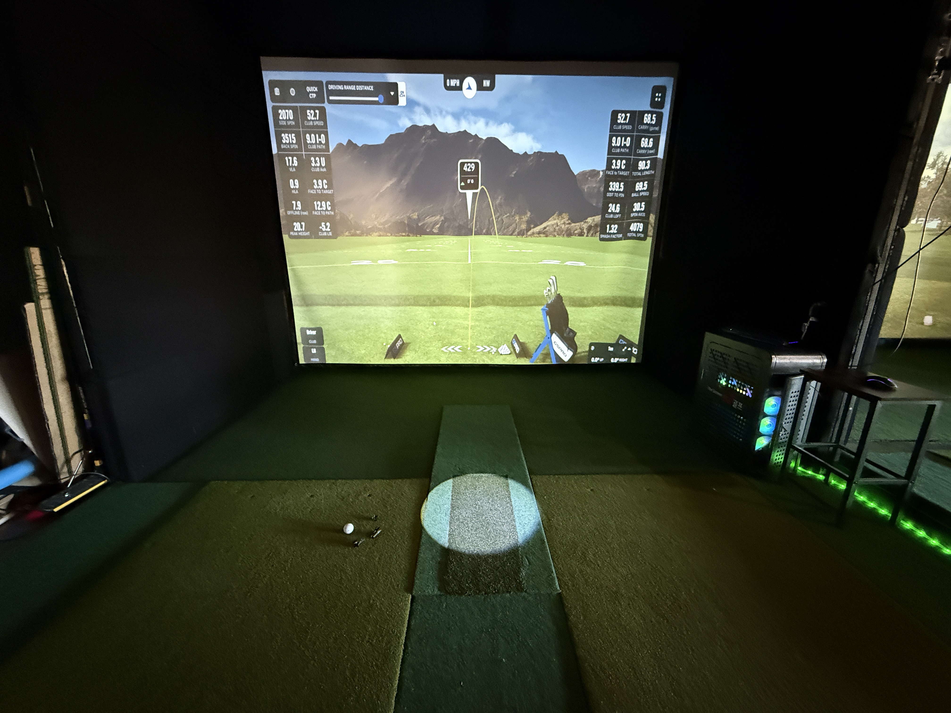 Head-on view of simulator bay with ball on tee and GSPro screen