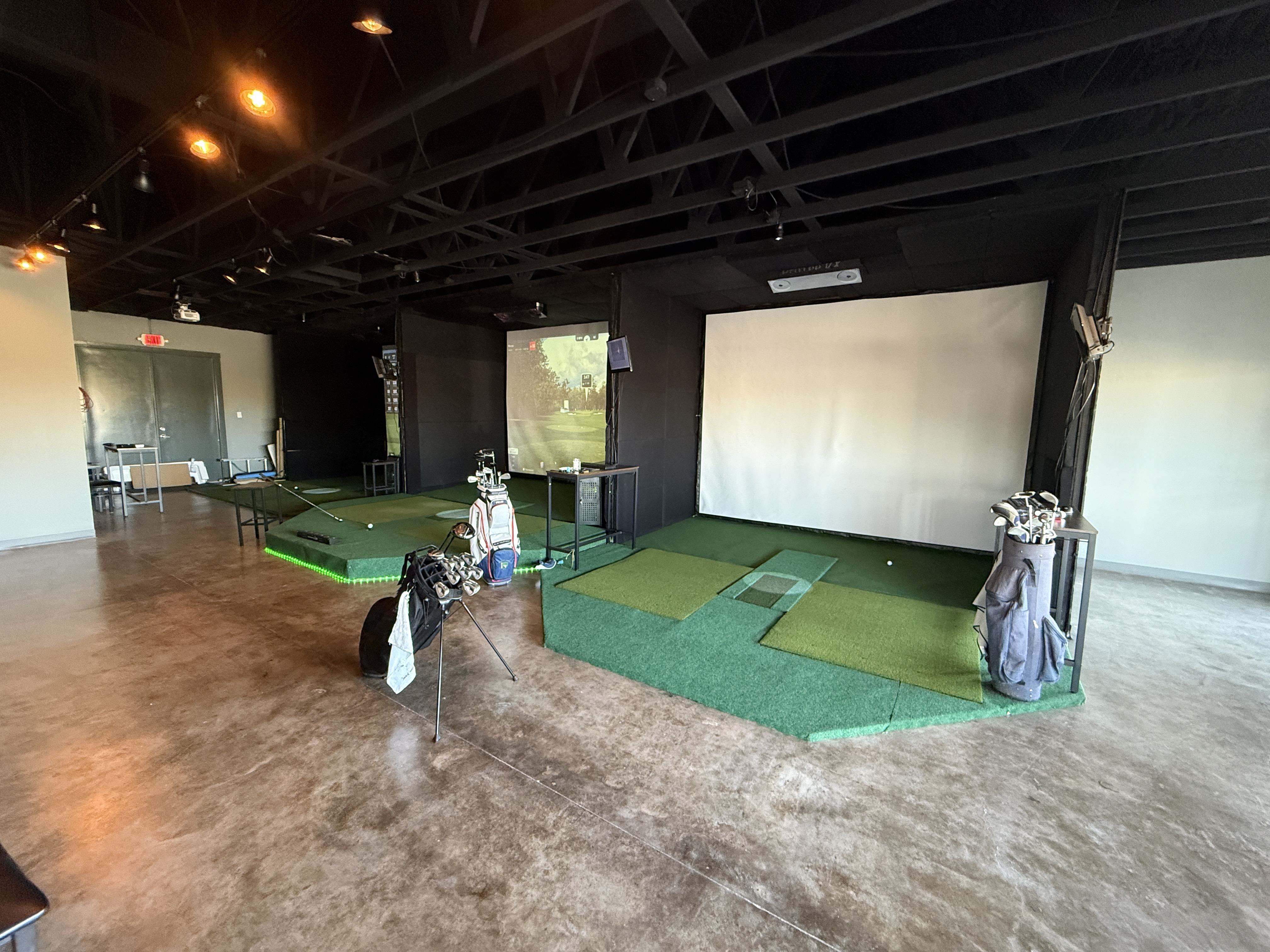 Wide shot of multiple simulator bays with golf bags and green LED lighting
